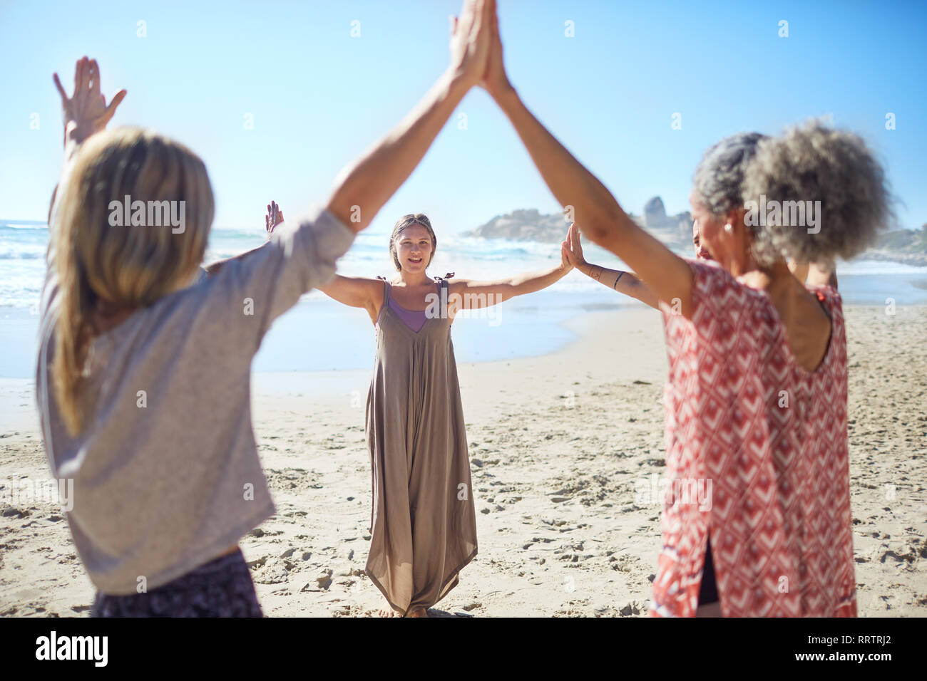 Le donne di unire le vostre mani in cerchio sulla spiaggia soleggiata durante il ritiro di yoga Foto Stock