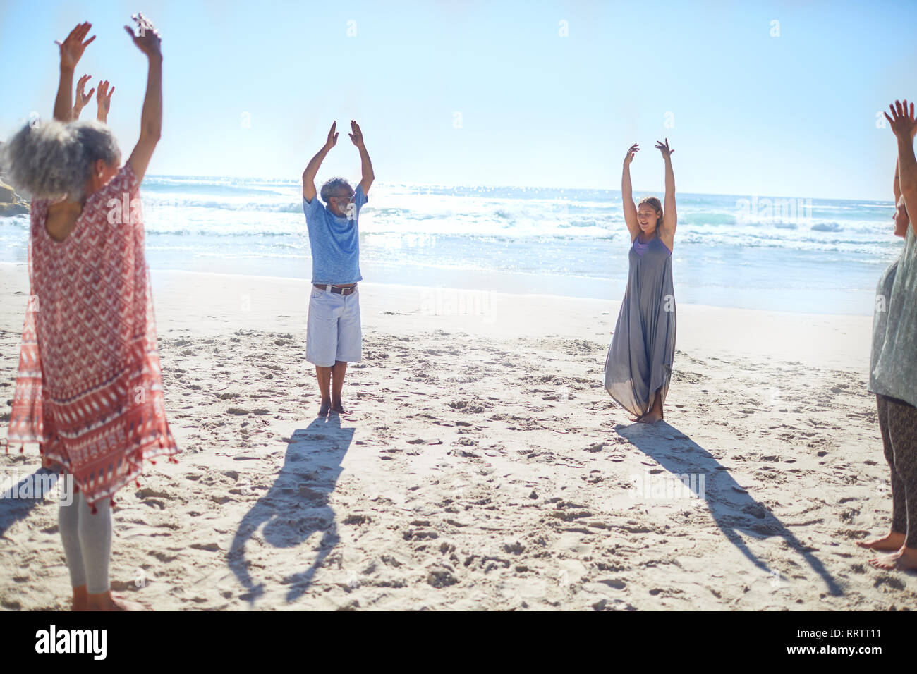 Gruppo in piedi con le braccia alzate in cerchio sulla spiaggia soleggiata durante il ritiro di yoga Foto Stock