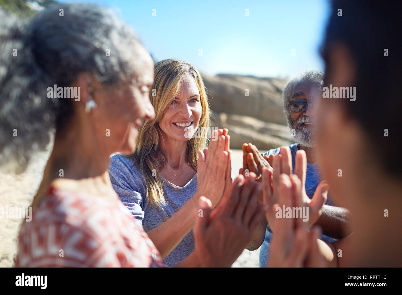 Gli amici con le mani incrociate in cerchio sulla spiaggia soleggiata durante il ritiro di yoga Foto Stock