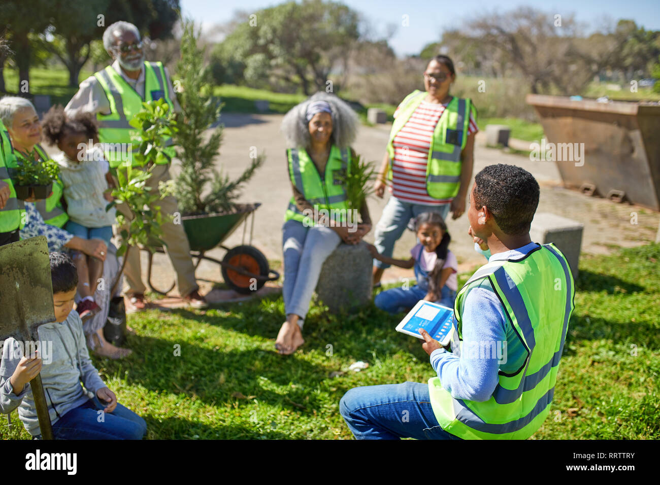 Uomo con tavoletta digitale volontari leader piantando alberi nel soleggiato parco Foto Stock