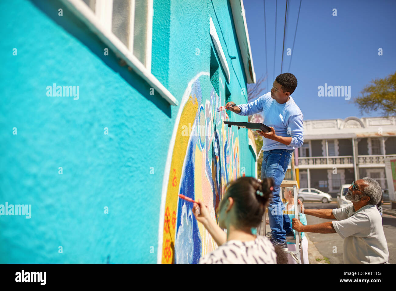 Volontari della comunità vibranti di pittura murale sulla soleggiata parete urbana Foto Stock