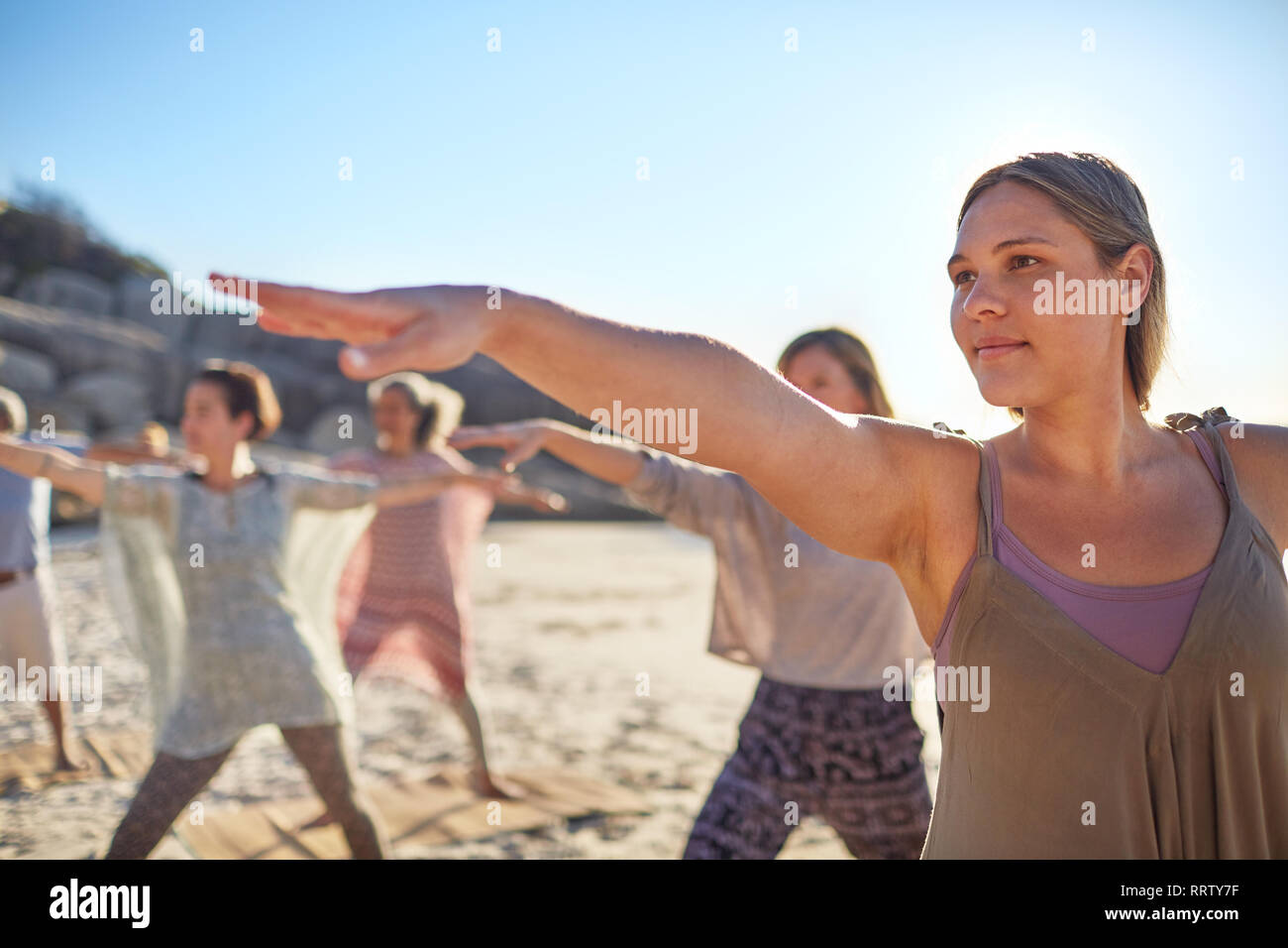 Fiducioso donna guerriero praticanti 2 pongono sulla spiaggia soleggiata durante il ritiro di yoga Foto Stock