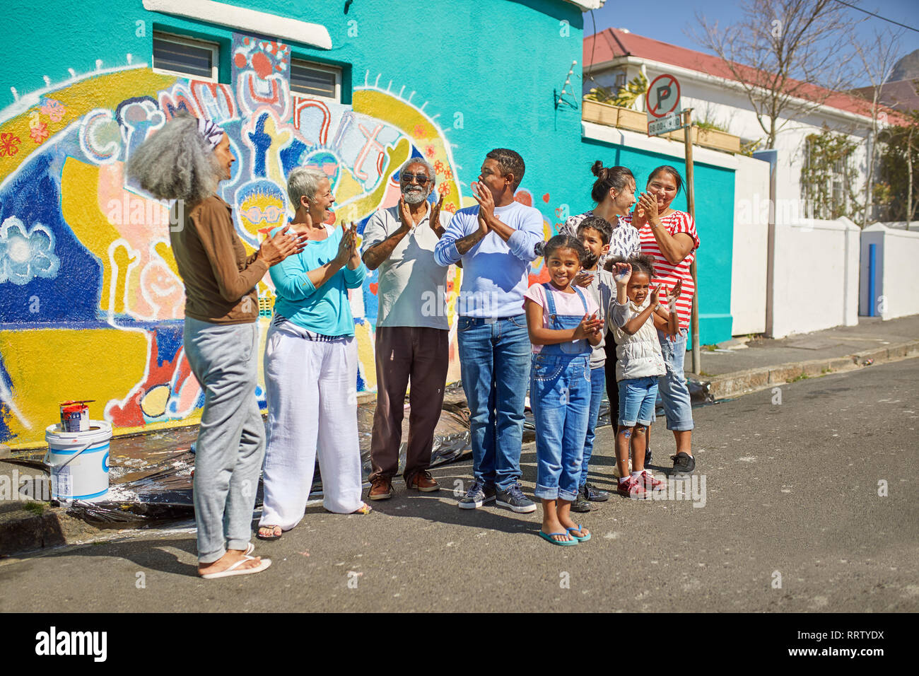 Felice volontari della comunità che celebra dipinto murale sulla soleggiata parete urbana Foto Stock