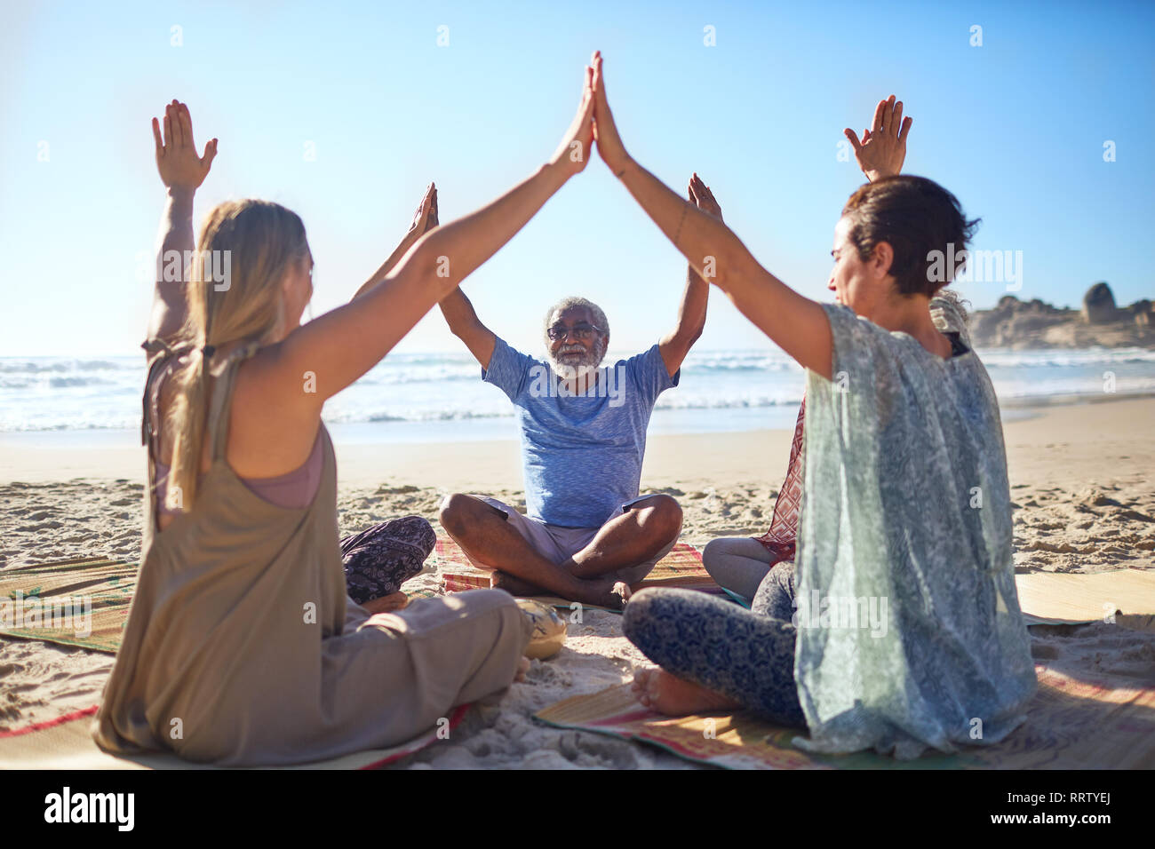 Gruppo di unire le vostre mani in cerchio sulla spiaggia soleggiata durante il ritiro di yoga Foto Stock
