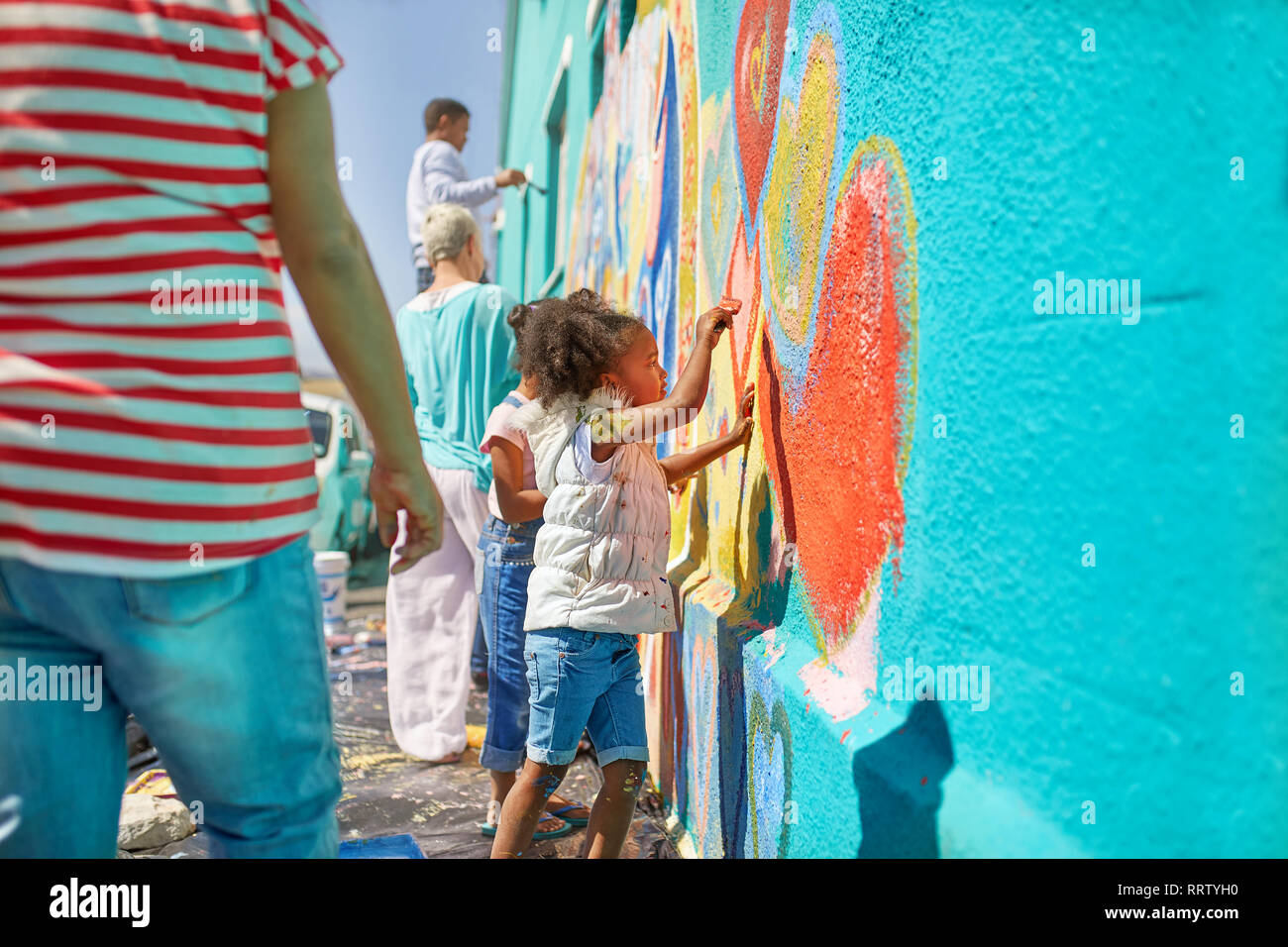Ragazza di volontariato vibrante di pittura murale sulla parete soleggiato Foto Stock