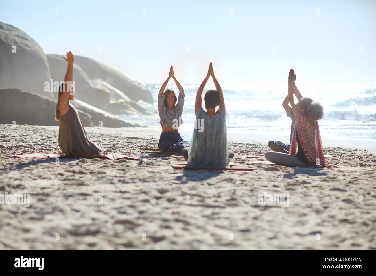 Serena la gente in cerchio meditando sulla spiaggia soleggiata durante il ritiro di yoga Foto Stock