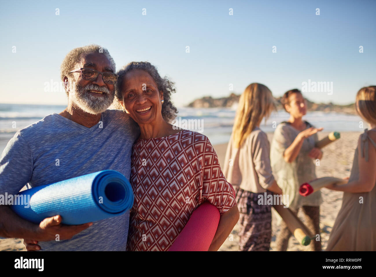 Ritratto felice coppia senior con Materassini da yoga sulla spiaggia soleggiata durante il ritiro di yoga Foto Stock