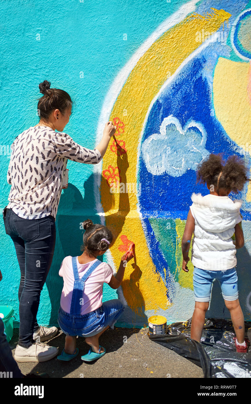 Madre e figlia volontari vibrante di pittura murale sulla parete soleggiato Foto Stock