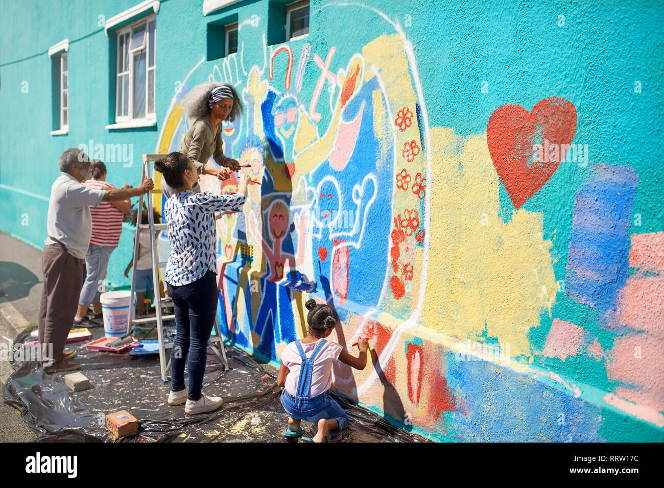 Volontari della comunità di pittura murale multicolore sulla soleggiata parete urbana Foto Stock