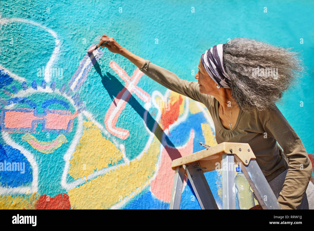 Senior donna vibrante di pittura murale sulla parete soleggiato Foto Stock
