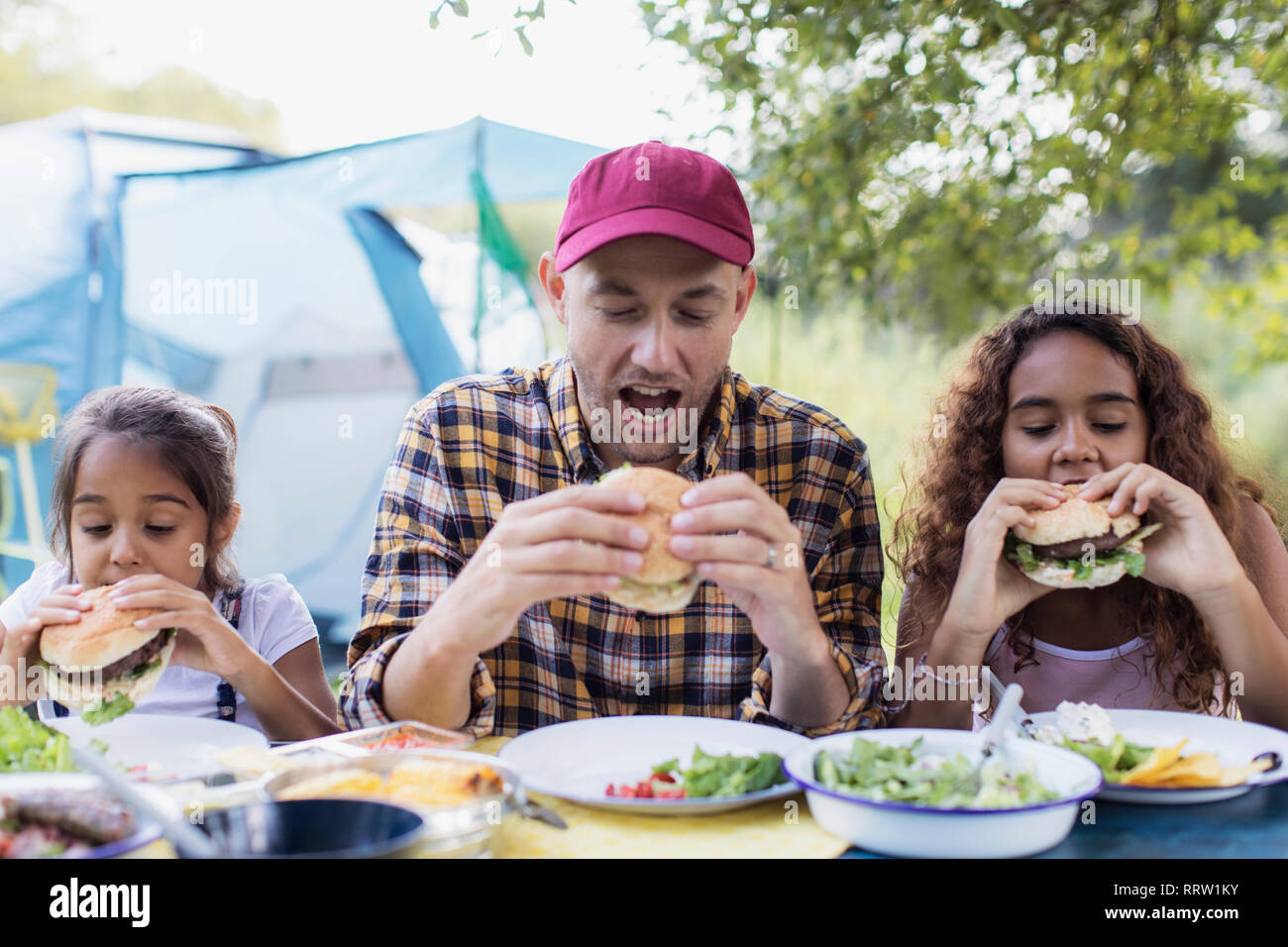 Padre e le figlie di mangiare hamburger barbecue al campeggio Foto Stock