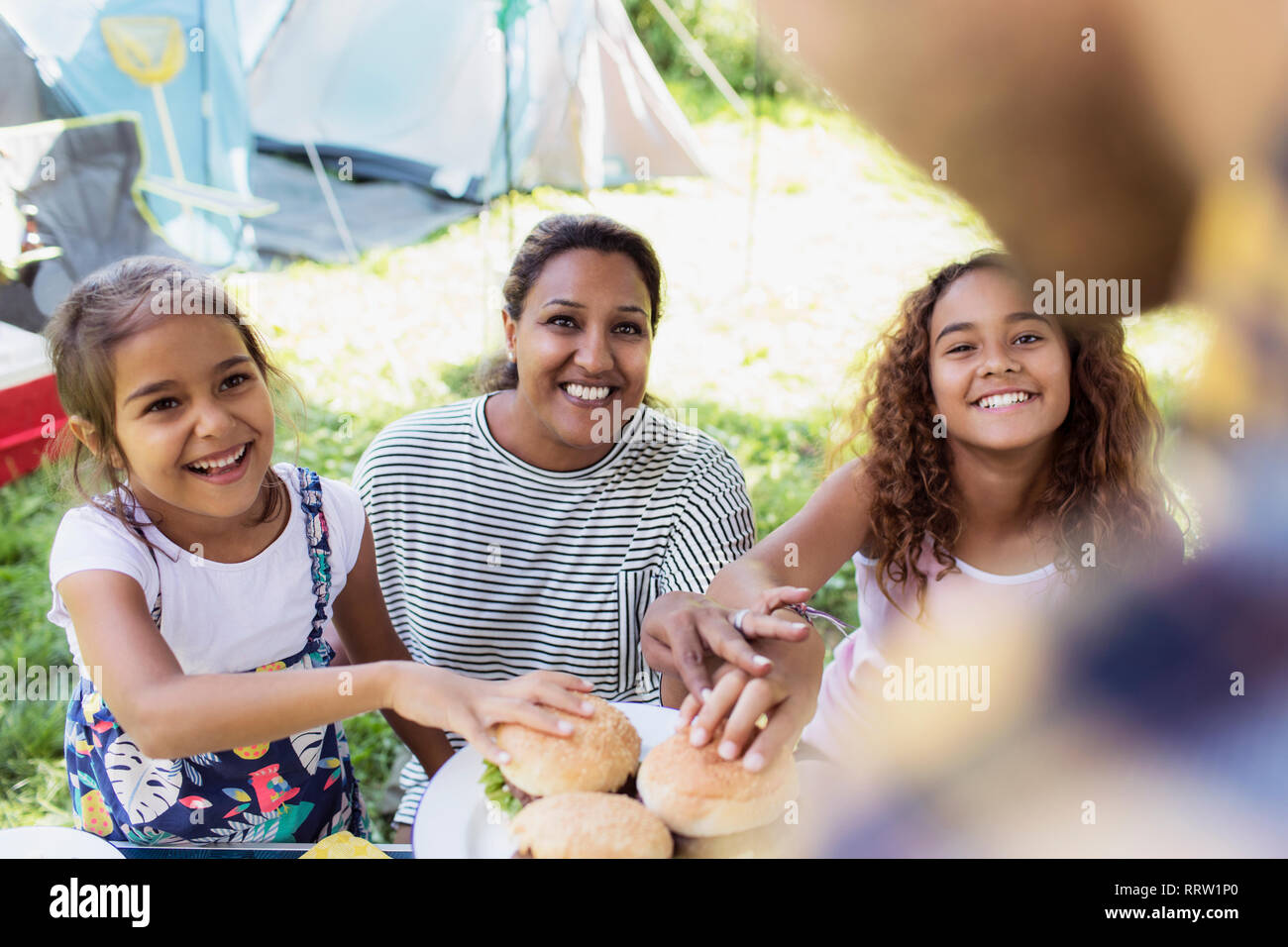 Padre che serve barbecue hamburger a ansiosi famiglia al campeggio Foto Stock