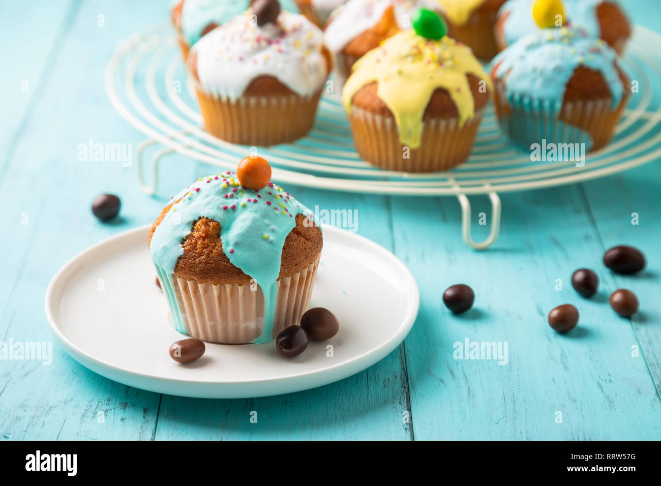 La pasqua o il compleanno tortine vetrate colorate con lo zucchero e un pizzico di cioccolato per una festa per bambini su una tavola di legno tabella turchese Foto Stock