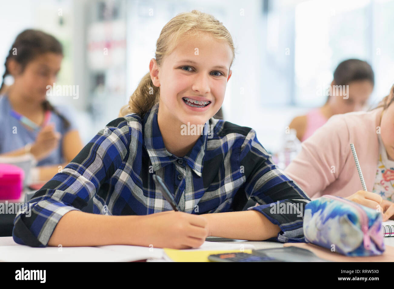 Ritratto sorride, entusiasta junior high school girl studente con bretelle in aula Foto Stock