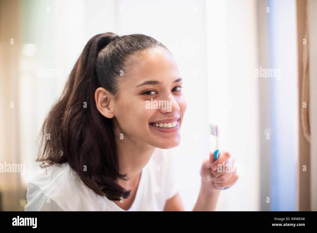 Ritratto sorridente, fiducioso donna spazzolare i denti in Specchio bagno Foto Stock