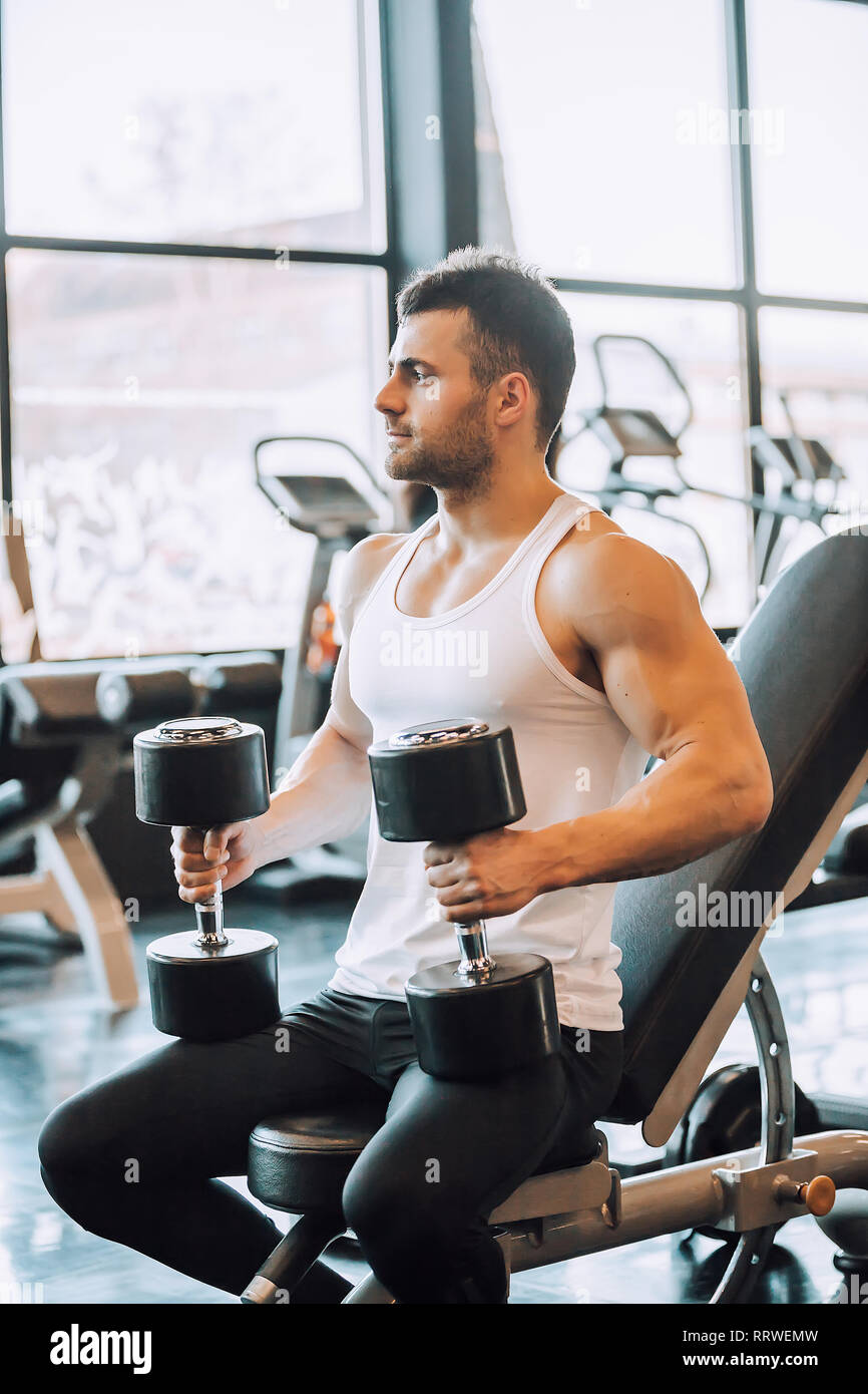 Determinato uomo muscolare esercizio con manubri in palestra - Immagine Foto Stock