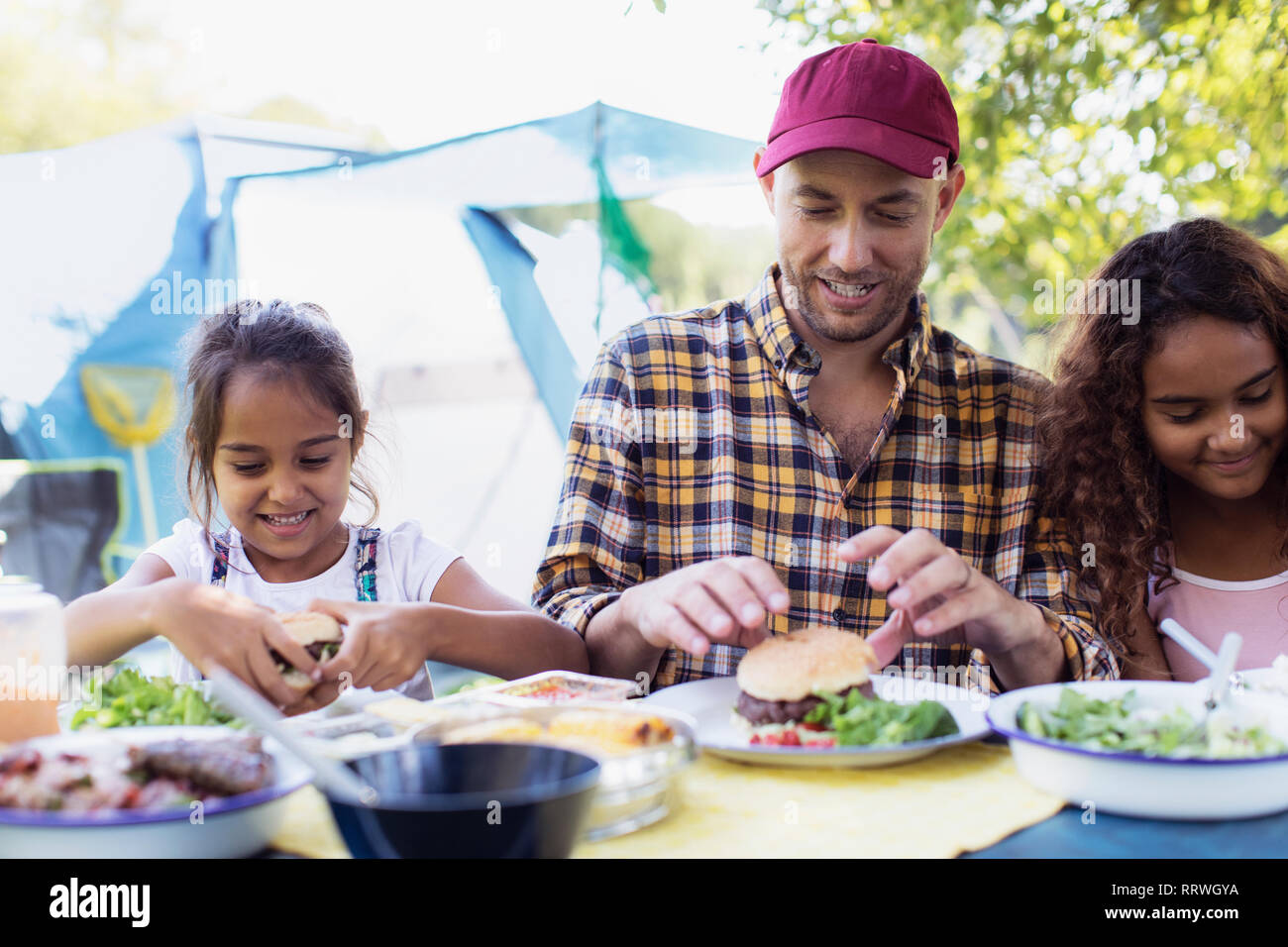 Padre e figlie godendo di hamburger pranzo al campeggio Foto Stock