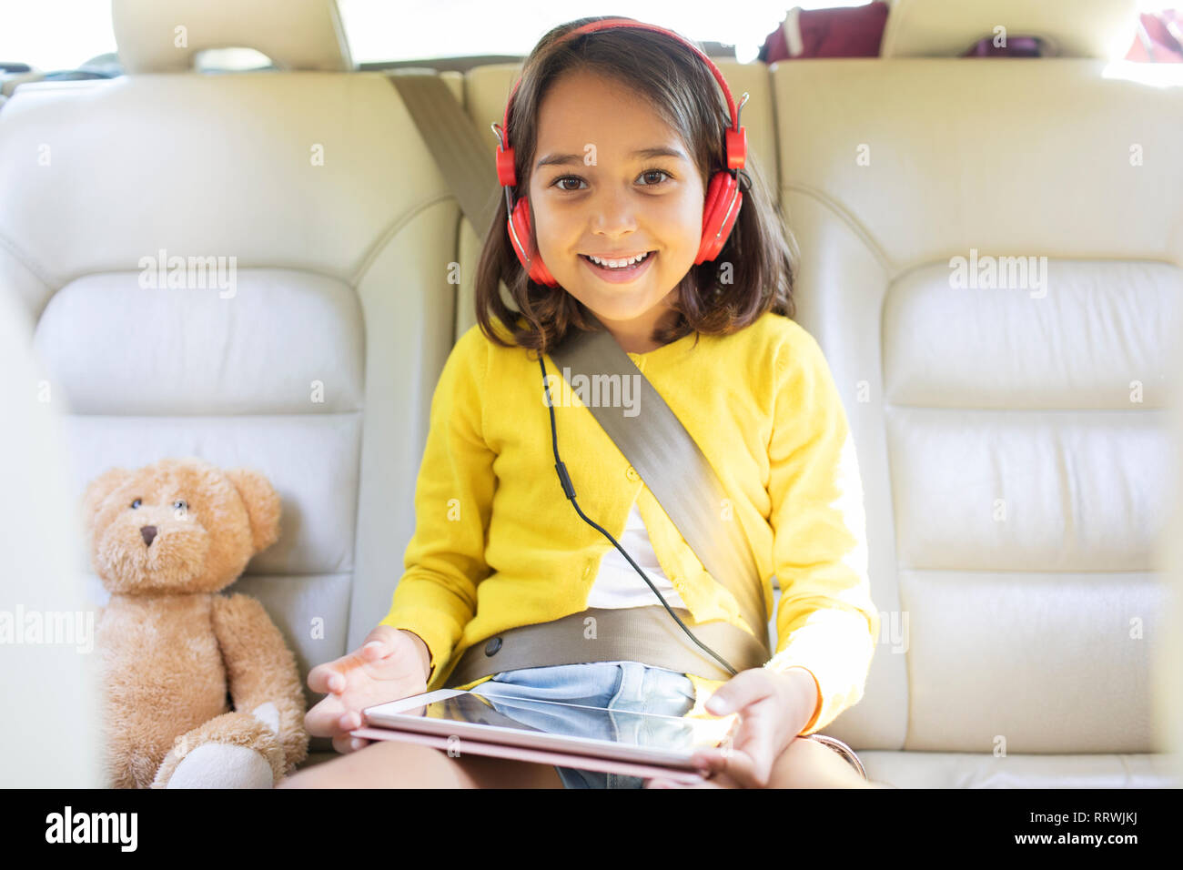 Ritratto sorridente, fiducioso ragazza guardare film con le cuffie e la tavoletta digitale nel sedile posteriore della macchina Foto Stock