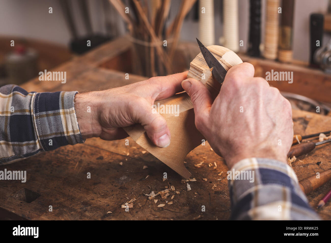 Le mani di un uomo con un coltello per affettare un piccolo pezzo di legno su un banco di lavoro Foto Stock