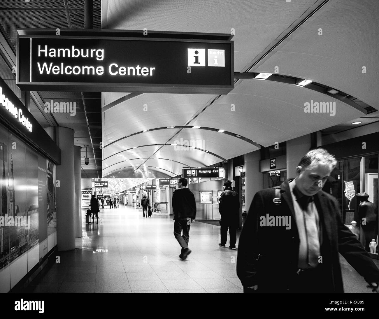 Amburgo, Germania - Mar 20, 2018: Adulto Uomo a camminare sotto il segno di Amburgo Welcome Center info turistiche punto interno aeroporto di Amburgo - bianco e nero Foto Stock