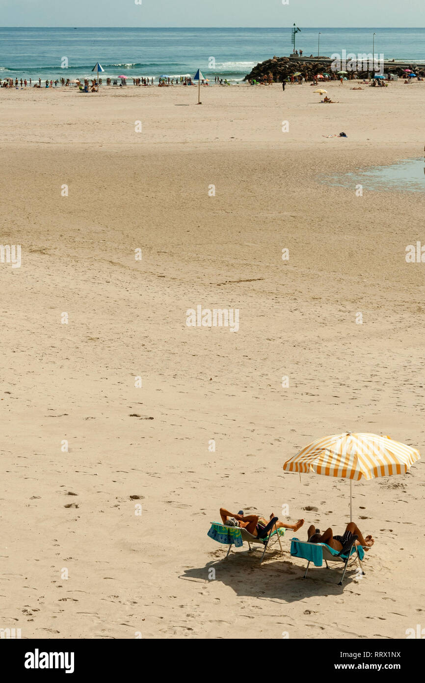 Giovane sotto gli ombrelloni sulla spiaggia, lontano dal popolo per essere tranquillo Foto Stock