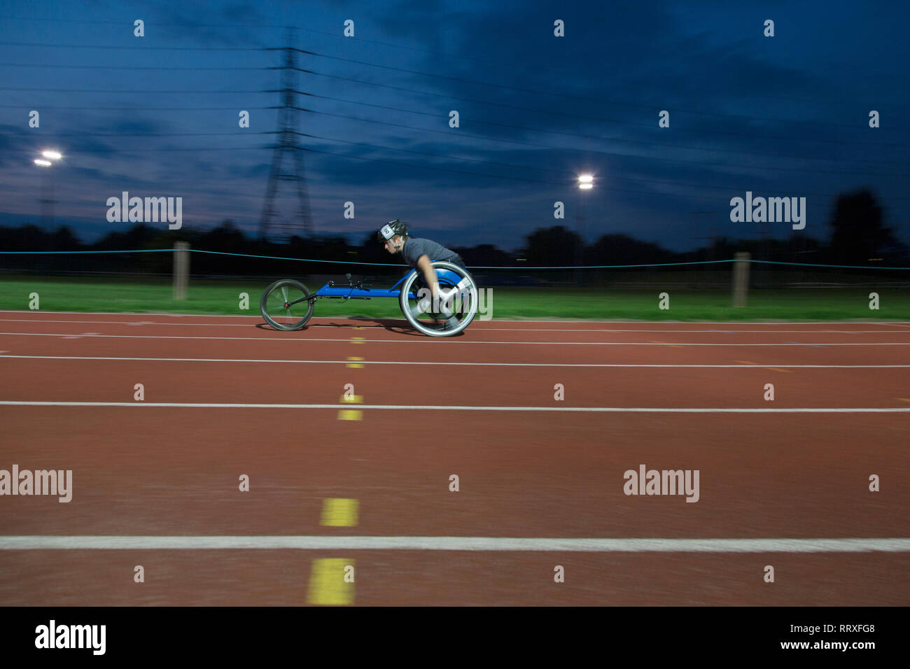 Femmina e giovane atleta paraplegico accelerando lungo la via dello sport in carrozzella gara in notturna Foto Stock
