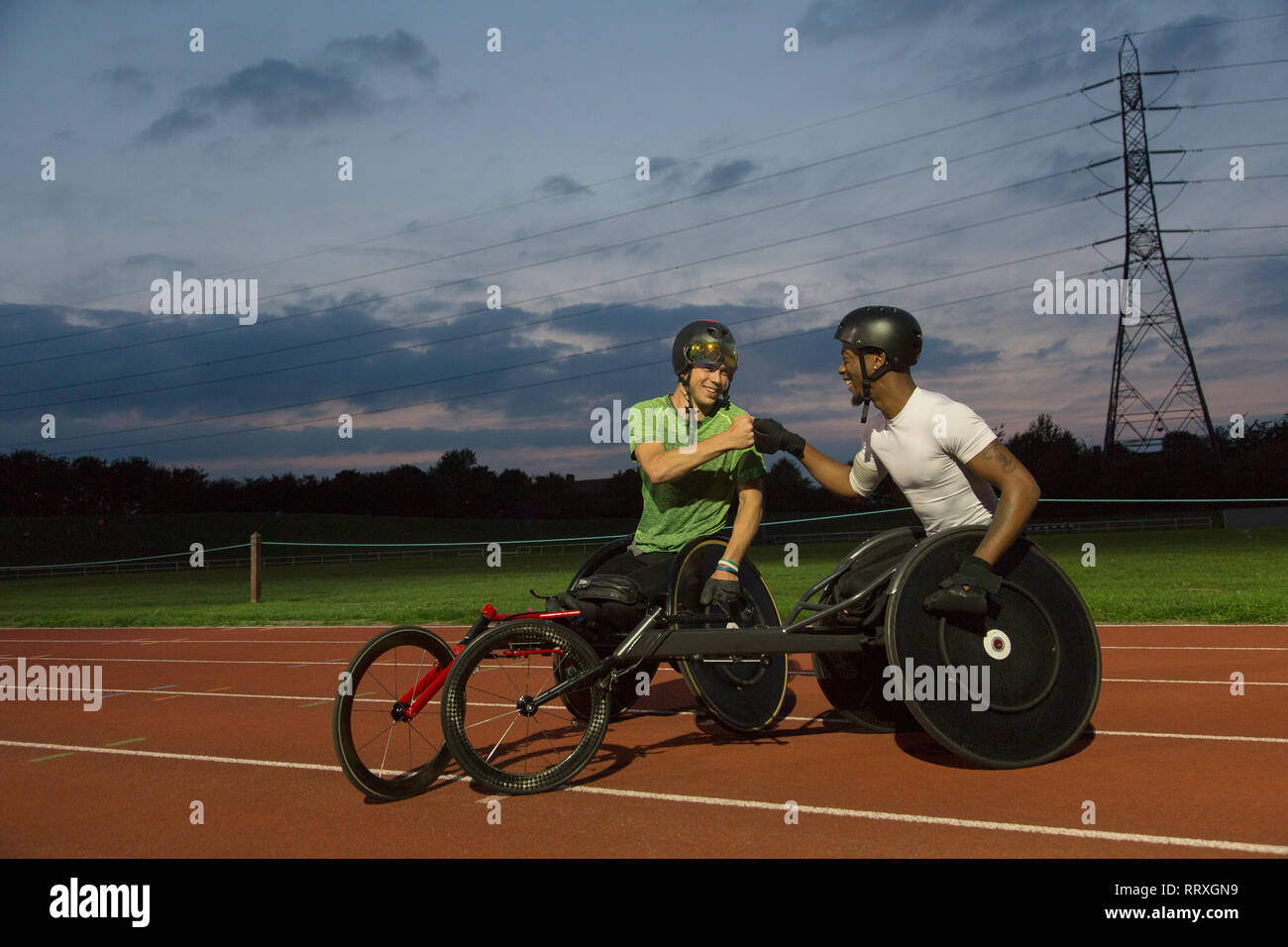 Gli atleti paraplegici fist bumping su sport via, formazione per una sedia a rotelle gara in notturna Foto Stock