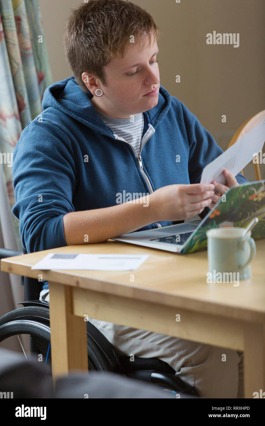 Giovane donna in sedia a rotelle il pagamento di fatture al laptop Foto Stock