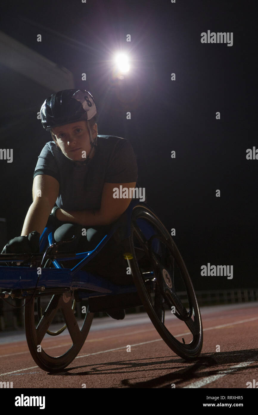 Ritratto determinata femmina e giovane atleta paraplegico formazione per sedia a rotelle gara su sport via di notte Foto Stock