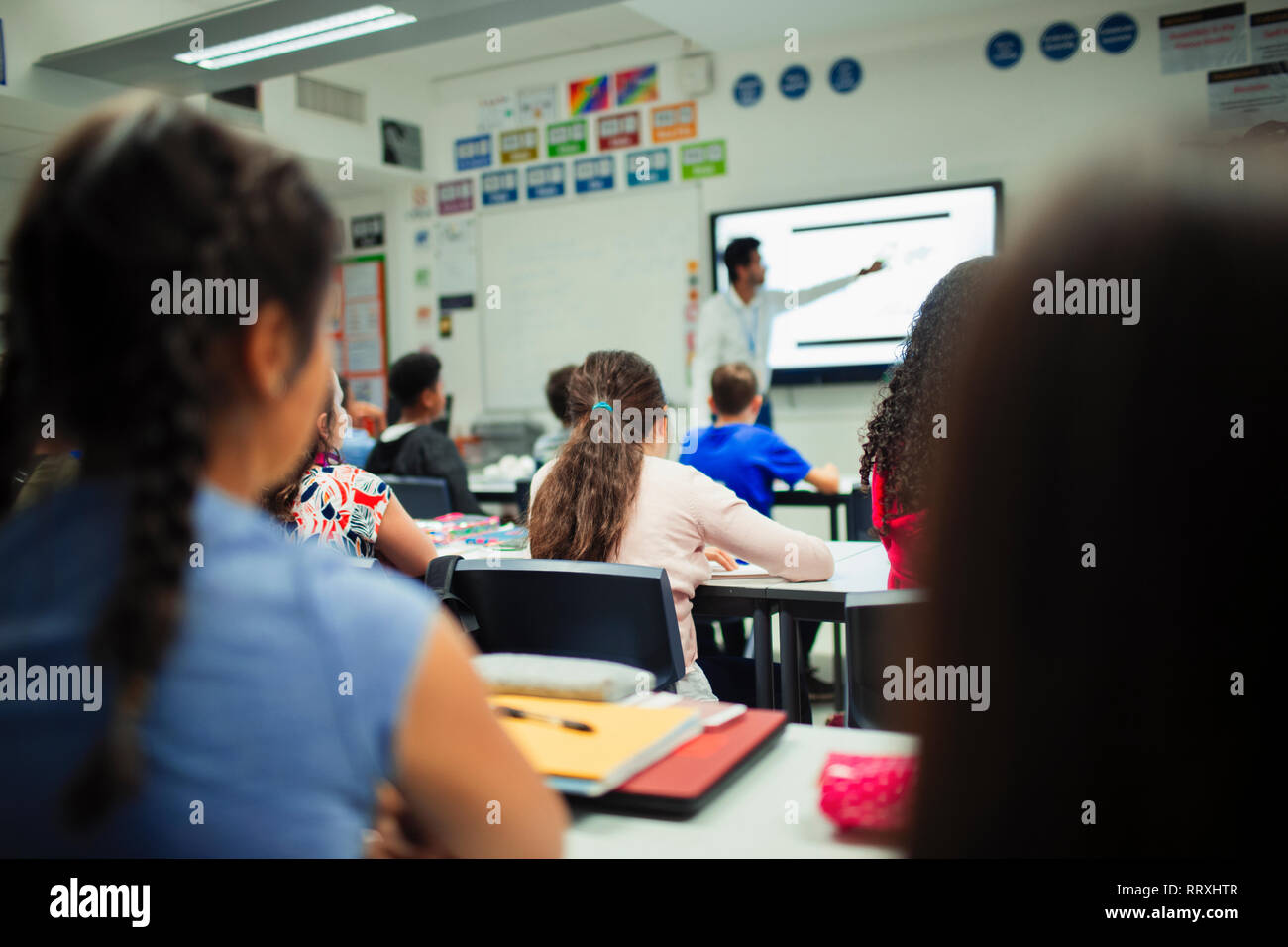 Studenti di scuola materna a guardare insegnante dare lezione a schermo di proiezione in aula Foto Stock