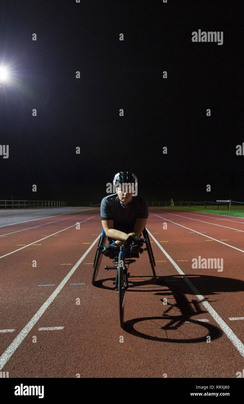 Ritratto fiducioso atleta paraplegico su sport via formazione per sedia a rotelle gara in notturna Foto Stock