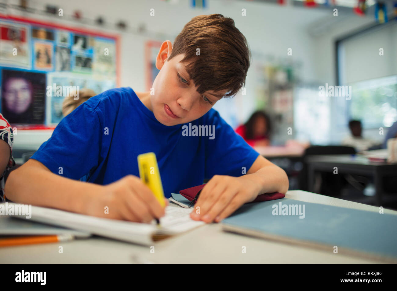 Focalizzato junior high school boy studente utilizzando evidenziatore, svolgendo compiti in classe Foto Stock