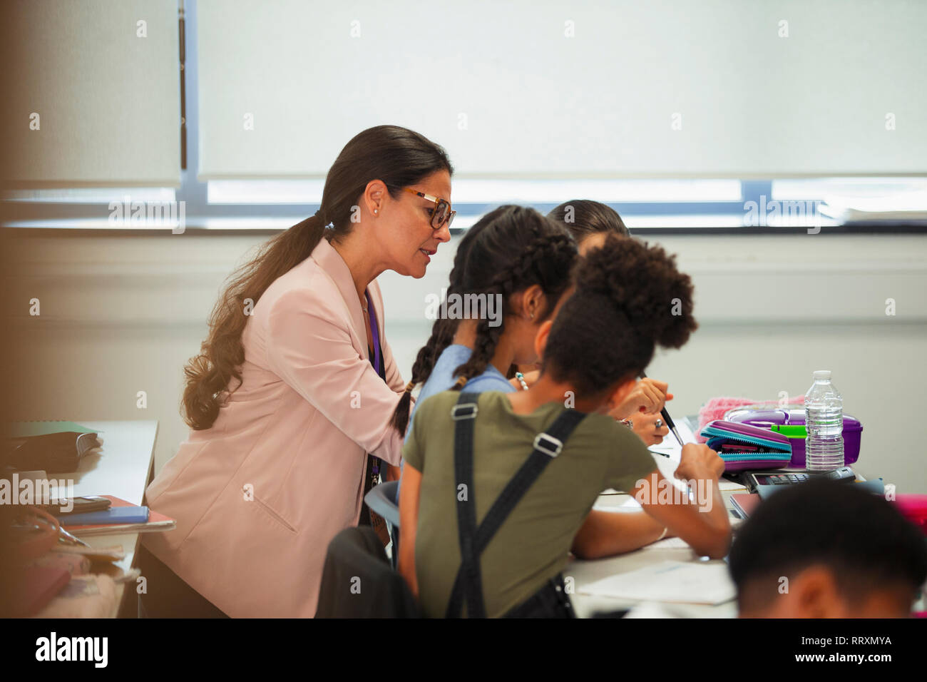 Docente aiutare studenti di scuola materna alla scrivania in aula Foto Stock
