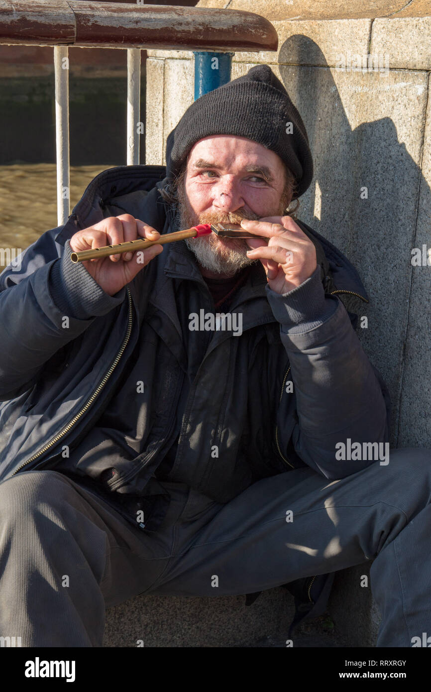 Un uomo senza tetto che fa musica su piccoli strumenti sulla South Bank di Londra, Inghilterra, Regno Unito in una giornata di sole a febbraio. Foto Stock