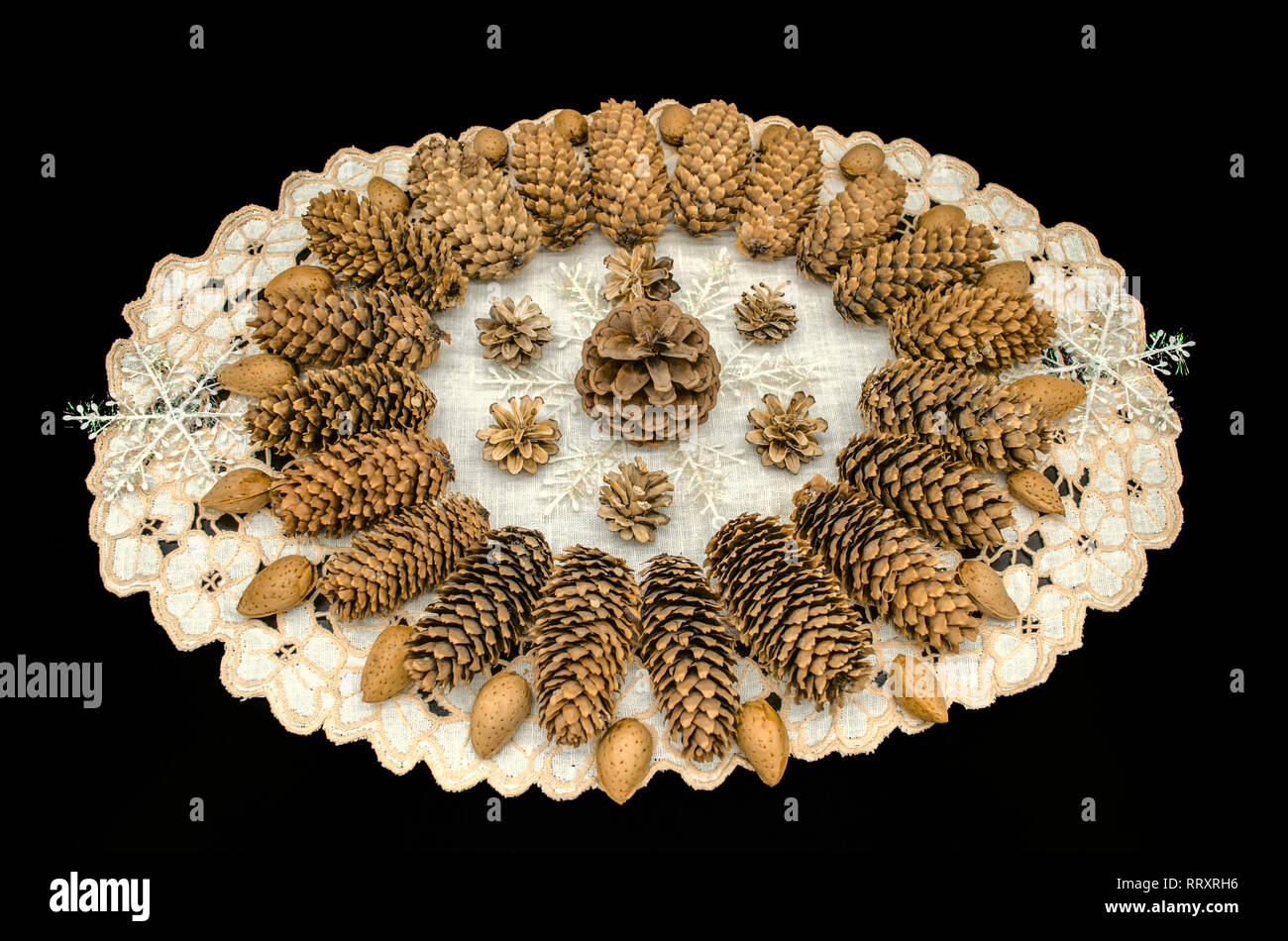 Sfondo nero con tovagliolo ricamato coperto con cornice ovale con pattern di coni di diverse razze, fiocchi di neve e mandorle sui bordi Foto Stock