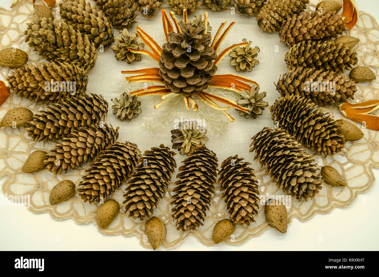 Bianco ricamato tovagliolo ondulate coperte con un pattern di fiocchi di neve asciutta e buccia di arancia circondato da coni di diverse razze e mandorle su una bianca Foto Stock