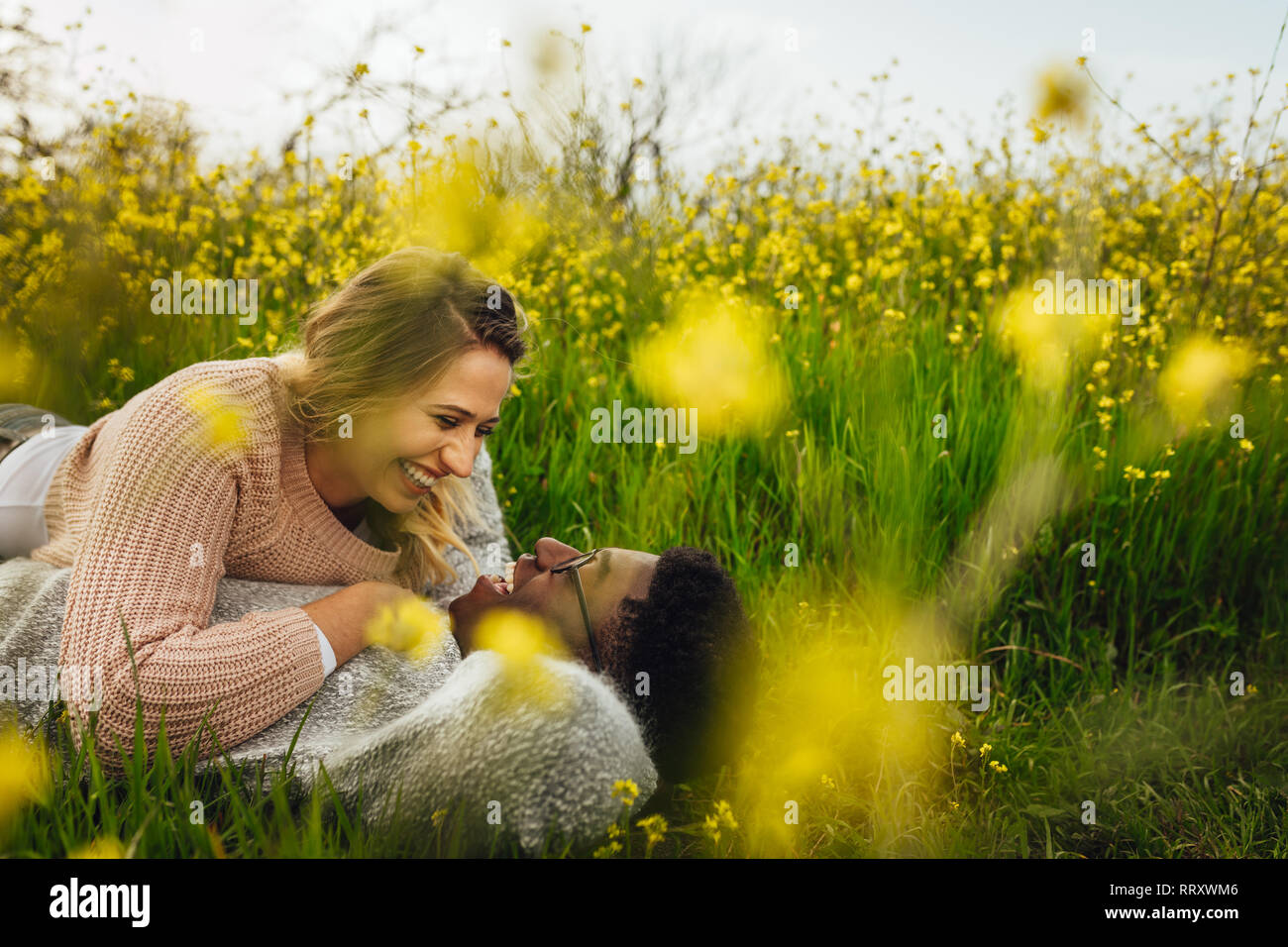 Bella donna sdraiata con il suo fidanzato sull'erba alta e sorridente. Coppia giovane sdraiati sull'erba guardando ogni altro e sorridente. Foto Stock