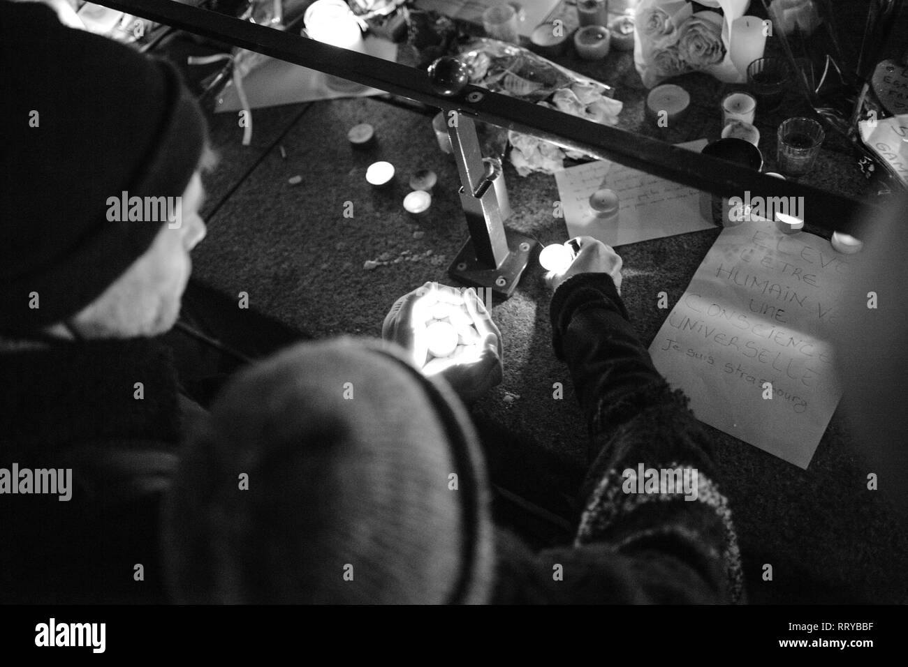 Strasburgo, Francia - Dic 13, 2018: uomo candela di protezione dal vento a veglia con più luce di candele fiori e messaggi per le vittime degli attentati Cherif Chekatt al mercatino di Natale Foto Stock