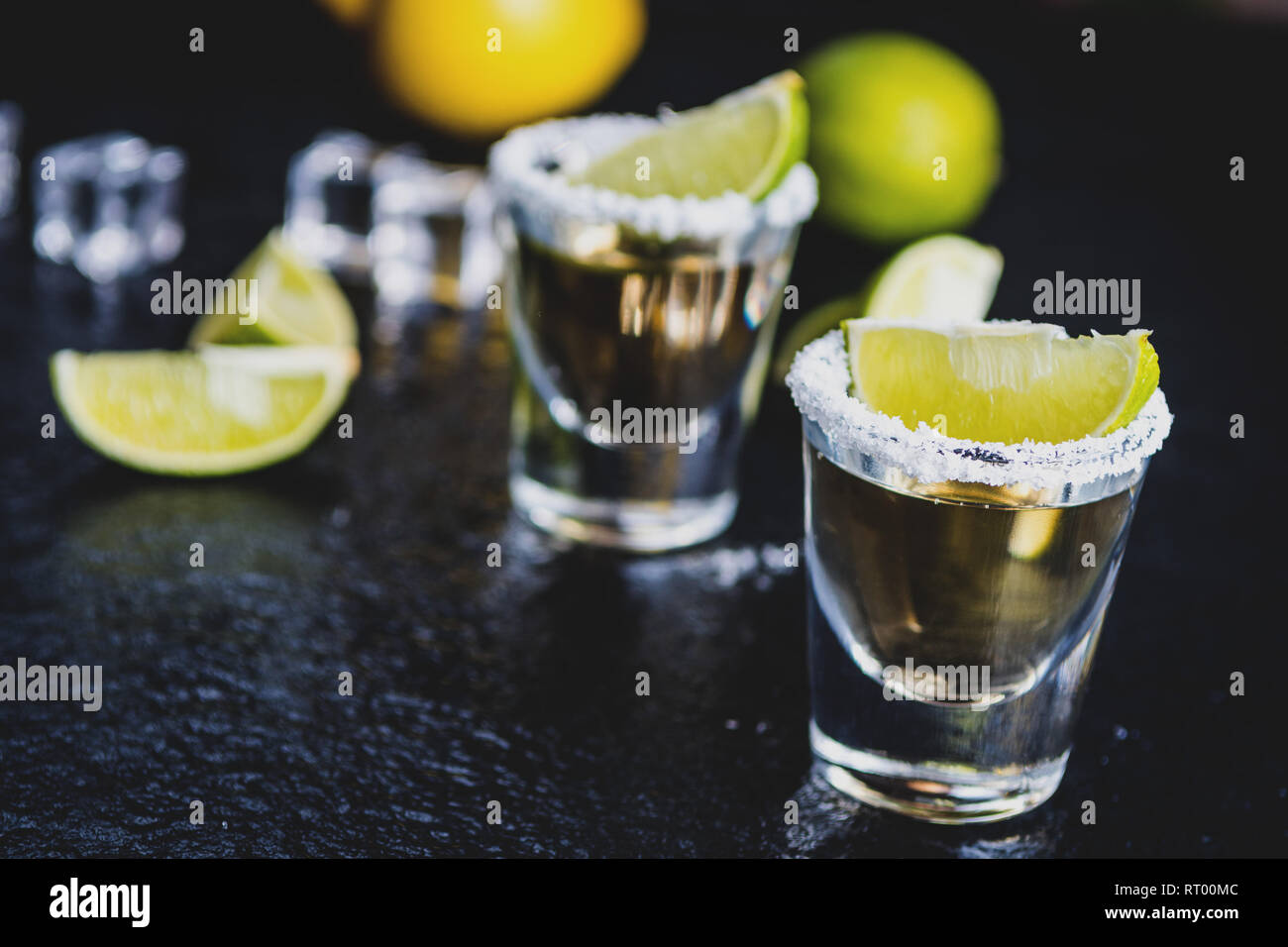 Tradizionale messicano Tequila con limone, calce,sale e il cubo di ghiaccio sulla pietra scura tabella tabella Foto Stock