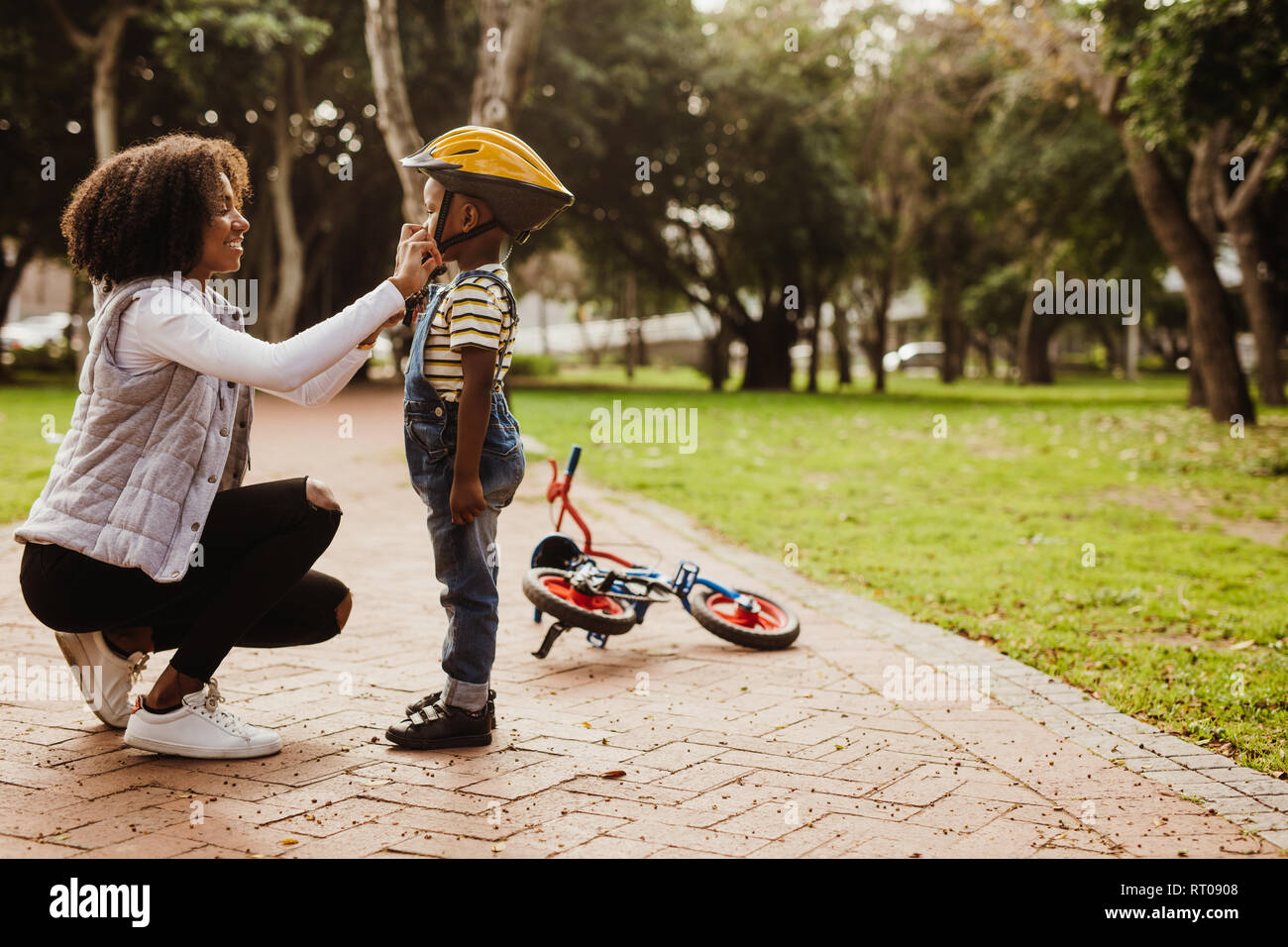 Madre aiutare figlio di indossare il casco per andare in bicicletta al parco. Ragazzo pronte da indossare il casco protettivo per avviare il ciclismo. Foto Stock