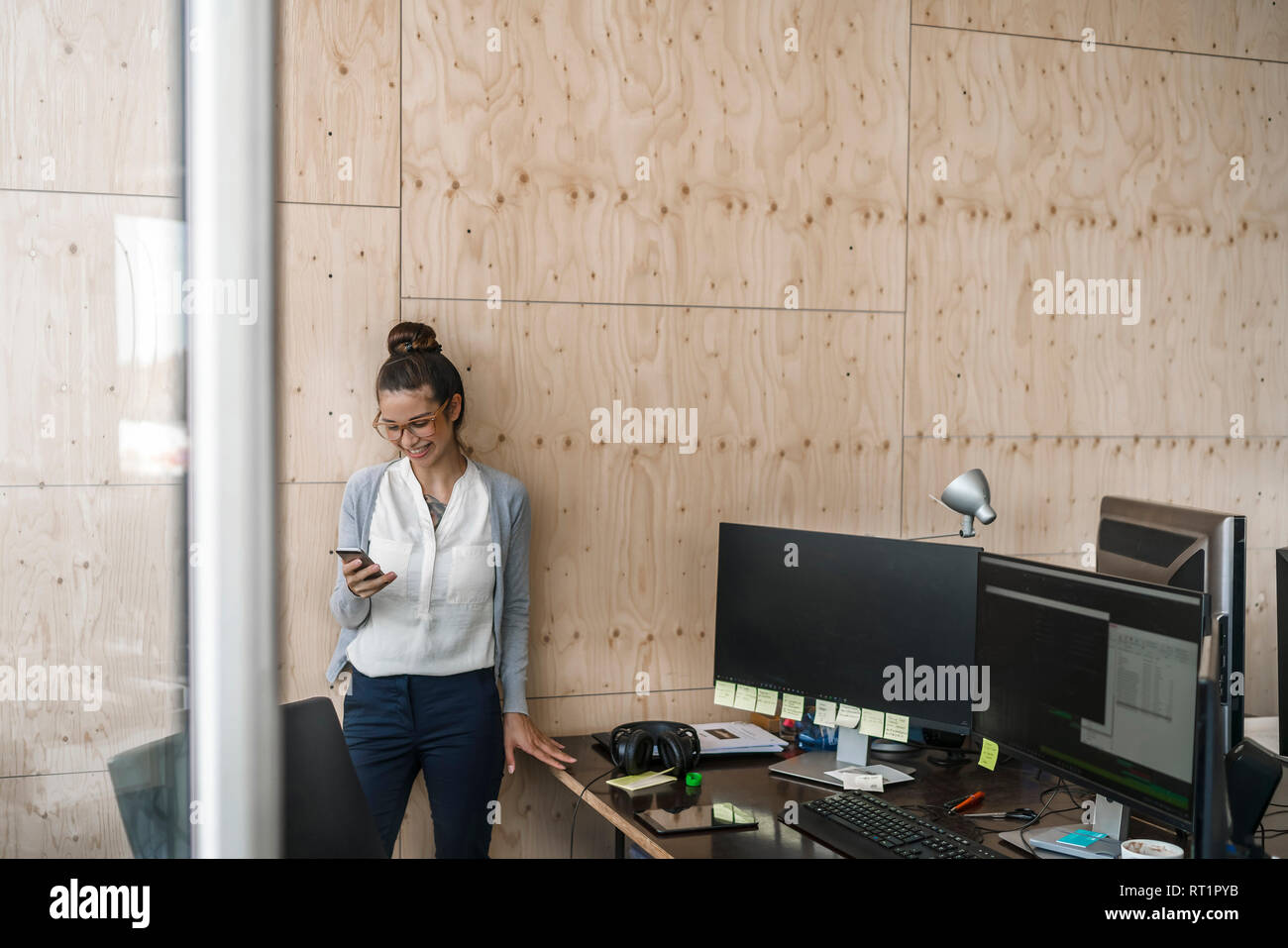 Giovane donna che lavorano in ufficio utilizzando smaftphone, ridendo Foto Stock