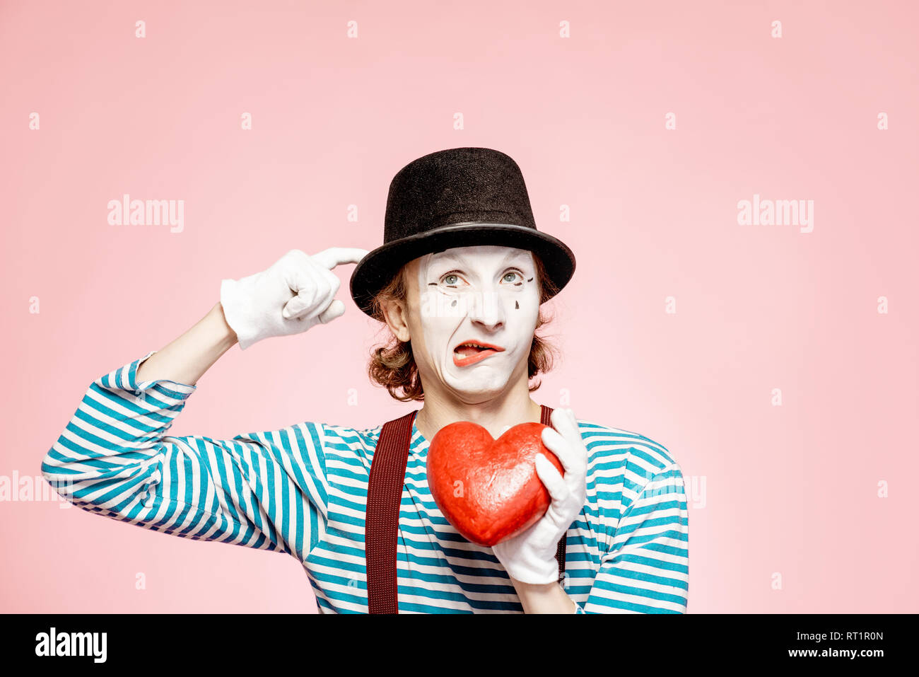 Ritratto di un attore come una pantomima bianca con il trucco per il viso in posa con cuore rosso su sfondo rosa Foto Stock