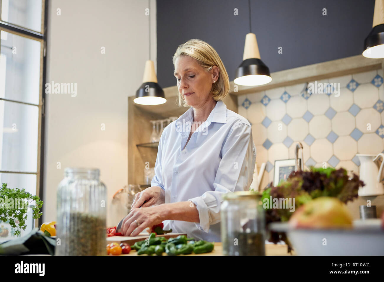 Donna matura tritare il peperone in cucina Foto Stock