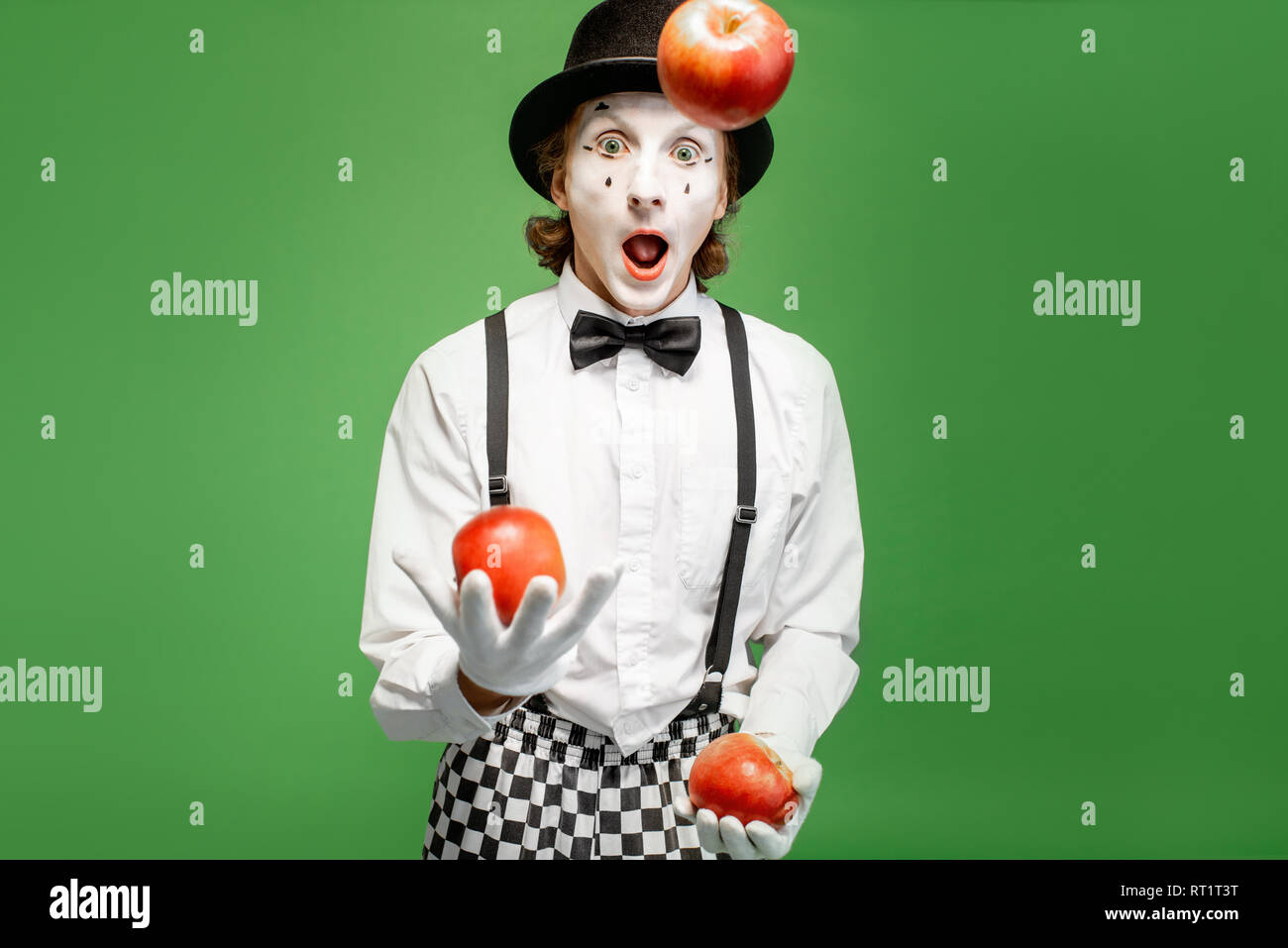 La pantomima bianca con il trucco per il viso giocoleria con mele sullo  sfondo verde in studio Foto stock - Alamy