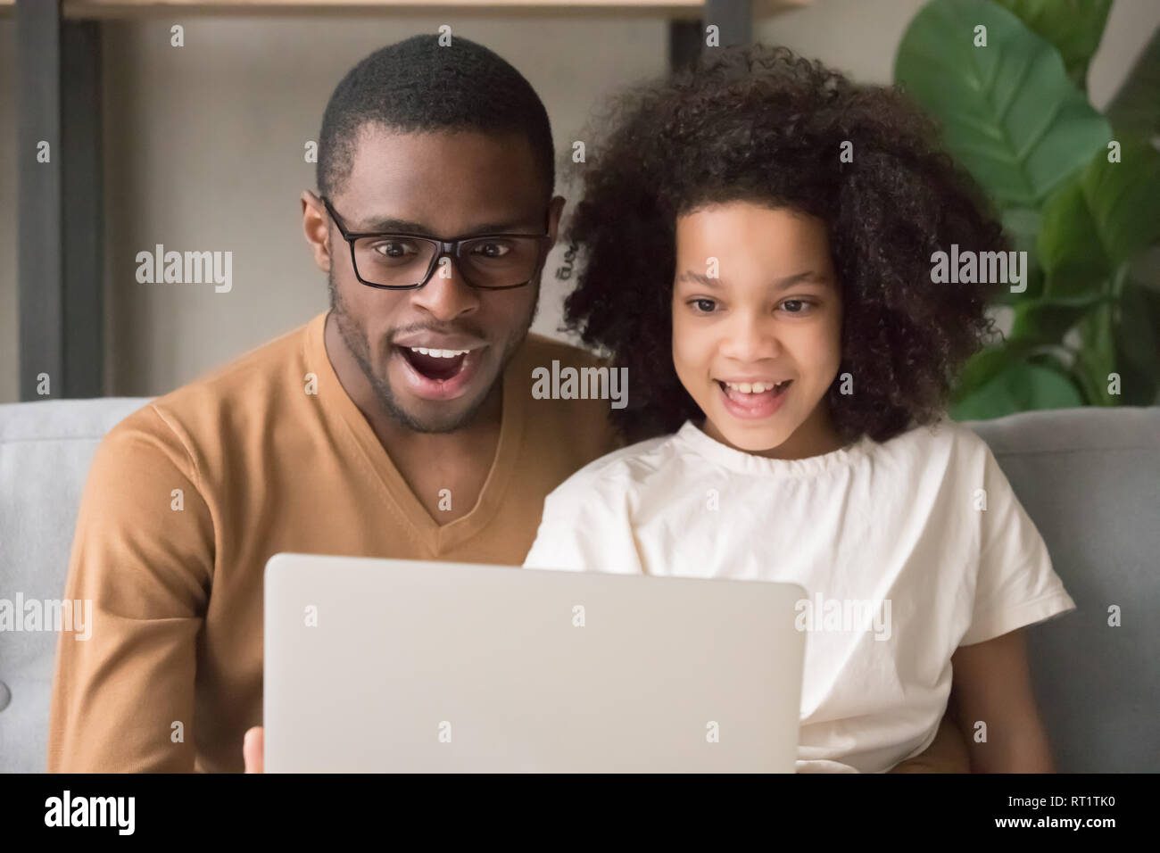 Sorpreso stupito papà nero e kid figlia guardando al laptop Foto Stock