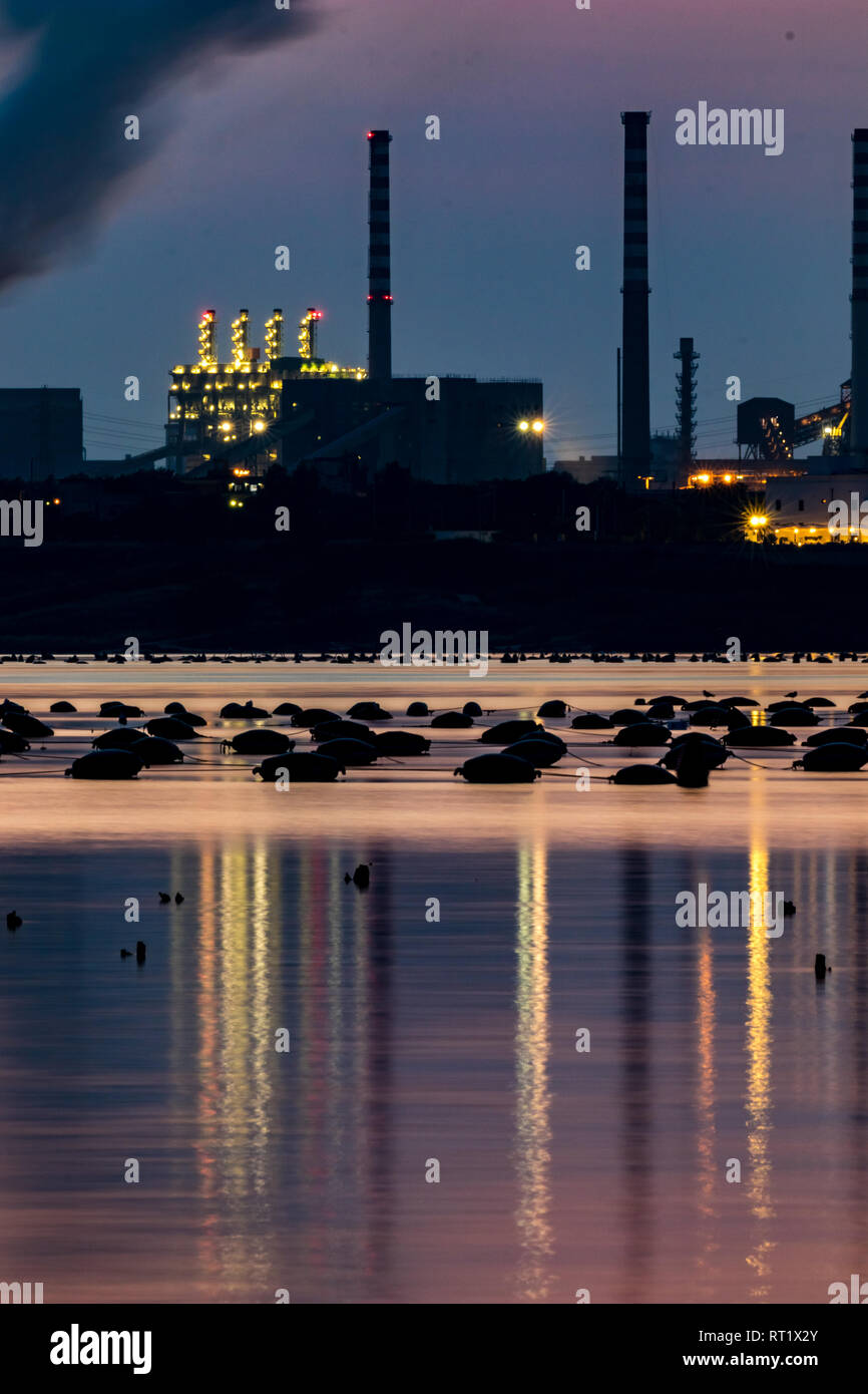 La fotografia notturna, una lunga esposizione immagine della zona industriale e la grande fabbrica di acciaio a Taranto, Italia con attrezzature di pesca nella parte anteriore e di acqua bella riflessi e colori del tramonto Foto Stock