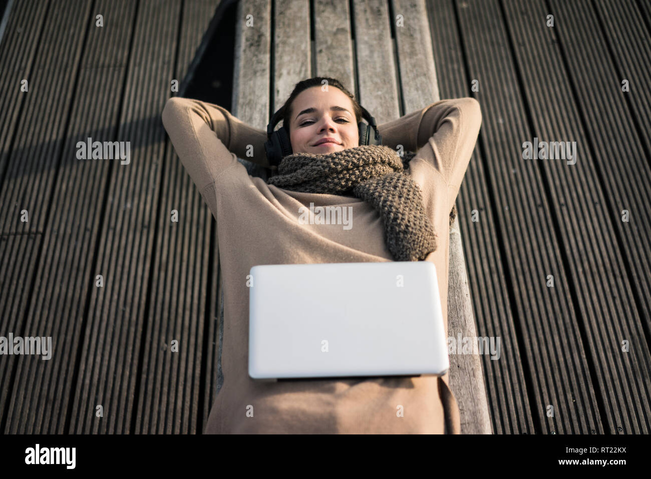 Ritratto di donna sorridente giacente sul banco di lavoro l'ascolto di musica con cuffie senza fili Foto Stock