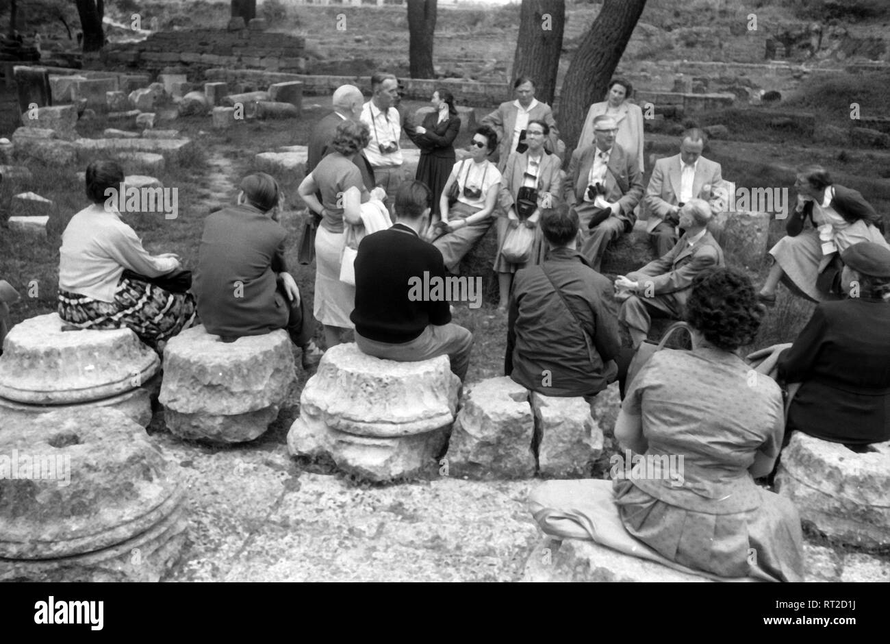 Griechenland, Grecia - Eine Touristengruppe macht eine kleine Pause und hört den Ausführungen des Reiseleiters zu in Griechenland, 1950er Jahre. Un gruppo di turisti di prendere un periodo di riposo e ascoltando le spiegazioni del loro tour guida in Grecia, 1950s. Foto Stock