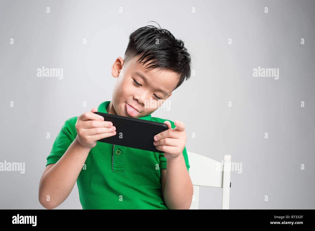 Ritratto di un divertito carino piccolo kid giochi su smartphone isolate su uno sfondo grigio Foto Stock