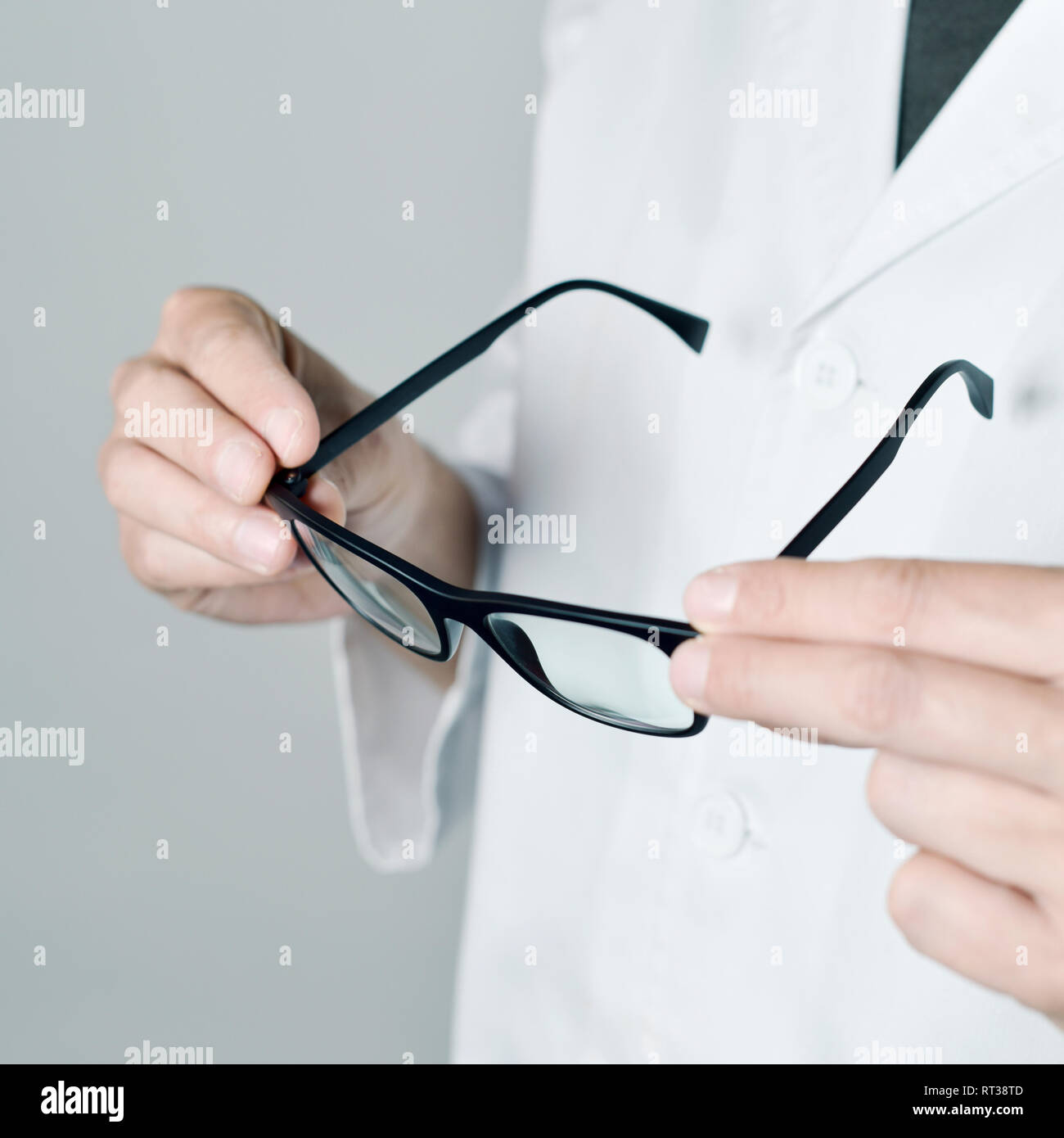 Primo piano di una giovane ottico caucasica uomo in camice bianco la verifica di un paio di occhiali Foto Stock